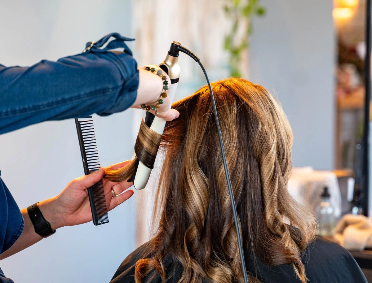 Stylist curling long balayage hair with a curling iron at SALT Salon + Spa, Antioch IL