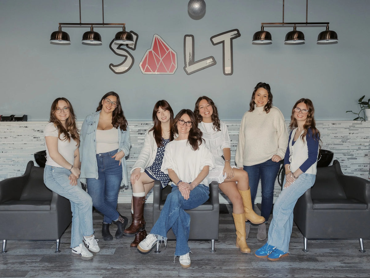 The SALT Salon + Spa team seated in front of the salon logo wall, Antioch, IL
